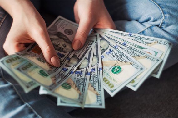 Photo of human hands holding $100 bills.